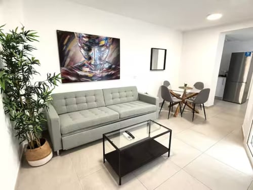 Luminoso apartamento moderno en Fuengirola con sofá gris, mesa de cristal, comedor y obras de arte contemporáneo