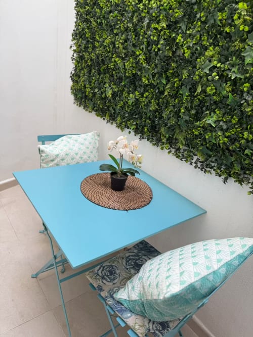 Luminosa zona de estar en apartamento de playa con mesa azul, orquídea en maceta y muro verde vivo en Fuengirola