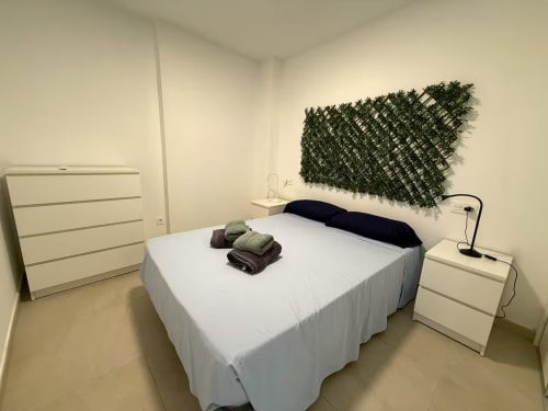 Dormitorio luminoso en apartamento frente al mar en Fuengirola con ropa de cama blanca, almohada negra, arte botánico y decoración blanca