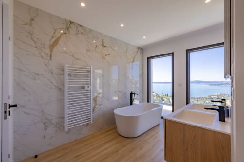 Salle de bain luxueuse de la villa PERLE D'AZUR avec murs en marbre, baignoire îlot et vue panoramique sur la Côte d'Azur