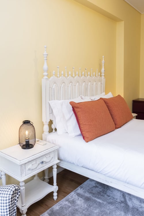 Bright yellow bedroom in RH Charming Apartments with white bed frame, terracotta pillows, and nightstand lamp in Braga