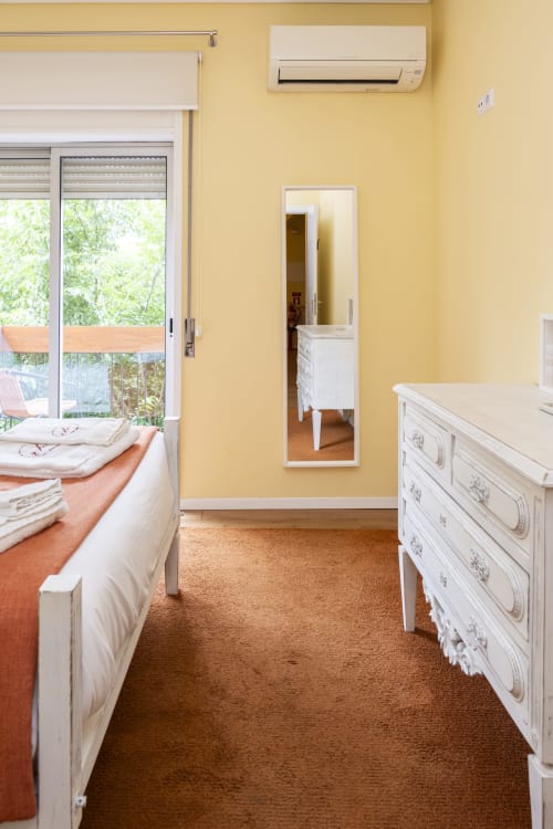 Bright yellow bedroom with white furniture, beds, mirrored wardrobe, and air conditioning unit at RH Charming Apartment
