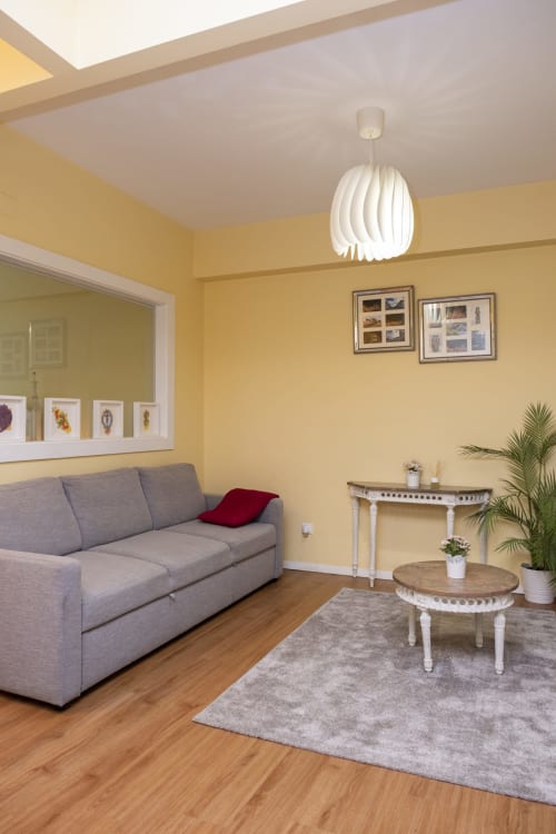 Bright yellow living room at RH Charming Apartments Braga with gray sofa, white pendant light, wooden floors