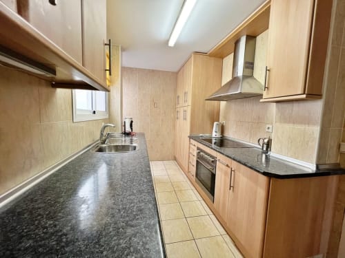 Cocina de galera moderna con encimeras de granito, gabinetes de madera y electrodomésticos de acero inoxidable en departamento frente al mar