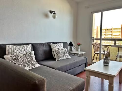 Salón moderno de apartamento frente al mar con sofá gris, cojines blancos y vistas al mar en Fuengirola