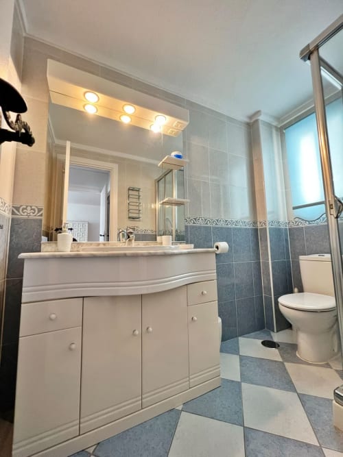 Baño moderno con vanitorio blanco, detalles en azulejos azules y ducha en apartamento frente al mar en Fuengirola