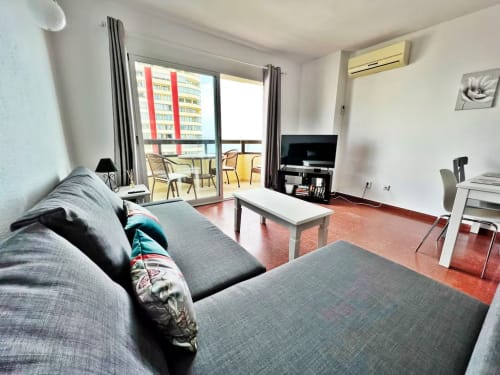 Apartamento moderno frente al mar en Fuengirola con sofá gris, mesa de centro blanca y balcón con vistas al océano y la ciudad