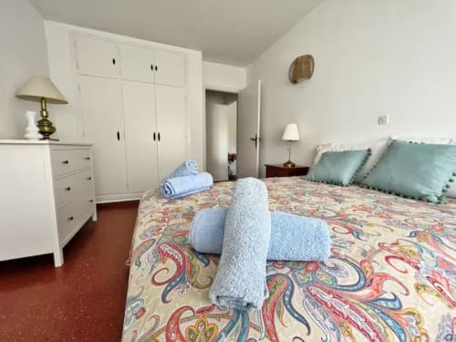 Dormitorio de apartamento frente al mar en Fuengirola con ropa de cama estampada, armarios blancos y almohadas turquesas