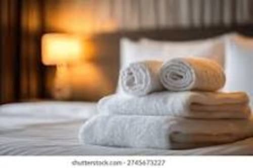 Rolled white and beige towels stacked on bed at Chalet école des Cîmes hotel in Bozel with warm lighting