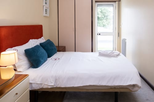 Modern bedroom at RH Charming Apartments in Braga with white bedding, red headboard, teal pillows, and city view door