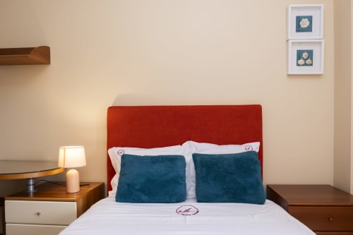 Modern bedroom at RH Charming Apartments in Braga with red upholstered headboard, teal pillows, white bedding, wooden