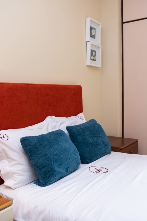 Modern bedroom in RH Charming Apartments Braga with red headboard, white bedding, teal pillows, and framed art on beige wall
