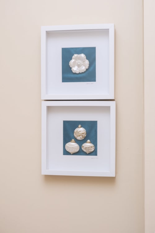 Two framed white botanical ornament artworks on teal backgrounds displayed vertically in RH Charming Apartments, Braga