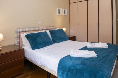 Modern bedroom at RH Charming Apartments in Braga with queen bed, blue pillows, white linens, and dark wood furniture