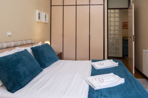Modern bedroom in RH Charming Apartments Braga with blue pillows, white bedding, and built-in wardrobe