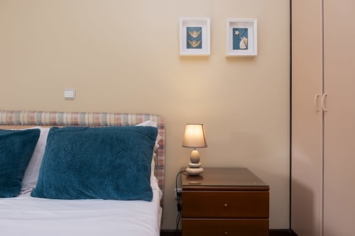 Cozy bedroom with teal pillows, striped headboard, bedside lamp, and two framed artworks in RH Charming Apartments, Braga