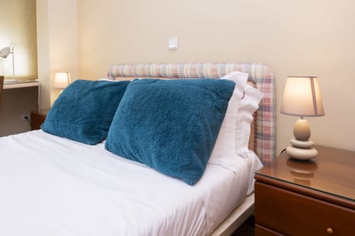 Cozy bedroom at RH Charming Apartments Braga with blue pillows, striped headboard, white bedding, and beside lamps