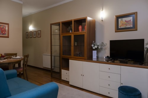 Modern apartment living room with blue sofa, TV, wooden furniture, and dining area in Braga