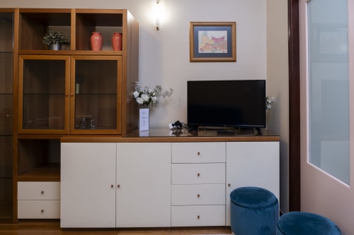 Modern living room in RH Charming Apartments Braga with wooden storage cabinet, flat-screen TV, blue ottoman seating, and