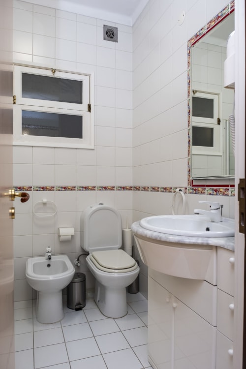 Modern bathroom with white tiles, bidet, toilet, round sink and decorative border at RH Charming Apartments in Braga