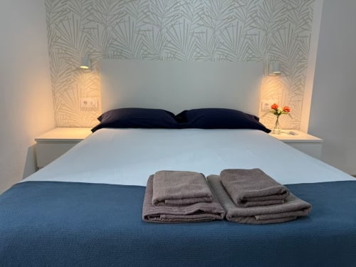 Moderno dormitorio en apartamento de Fuengirola con cama matrimonial, almohadas oscuras, toallas dobladas, mesitas con lámparas y decoración estampada