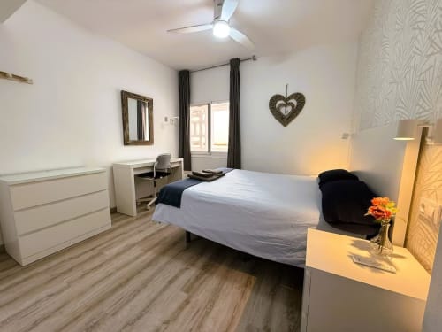 Moderno dormitorio en apartamento de Fuengirola con cama blanca, escritorio, cómoda, ventilador de techo y acceso a balcón