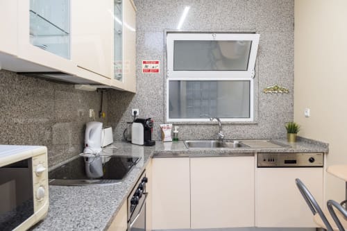 Compact kitchen in RH Charming Apartment São Victor, Braga with gray tile backsplash, cream cabinets, and city view window