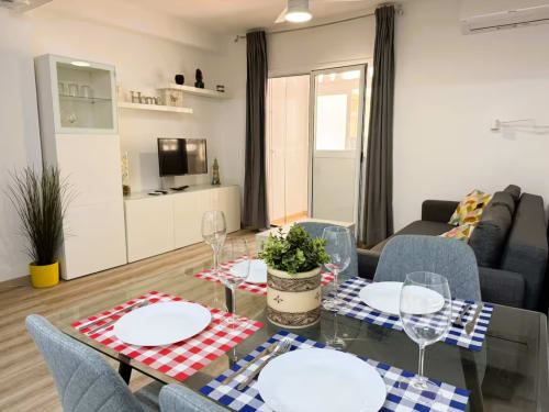 Comedor y salón moderno en Fuengirola con mesa lista, sofá gris, TV y acceso a balcón