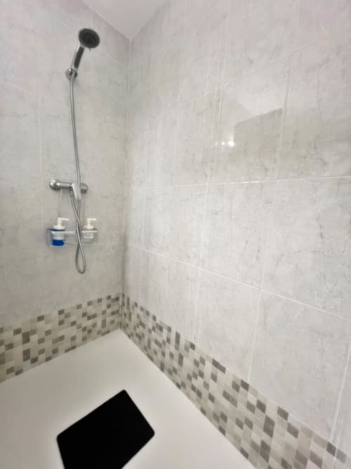Moderna cabina de ducha con azulejos efecto mármol, alcachofa de mano y cenefa de mosaico decorativo en apartamento de Fuengirola