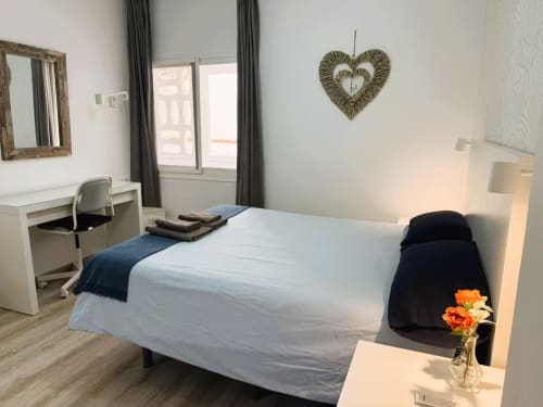 Moderno dormitorio en apartamento de Fuengirola con cama doble, escritorio, espejo, decoración en forma de corazón y acceso a balcón