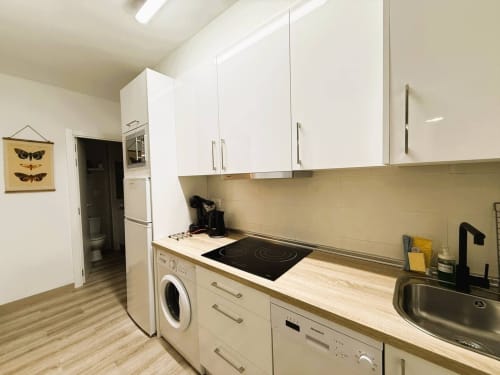 Cocina moderna en apartamento de Fuengirola con armarios blancos, encimera de madera, placa de cocción eléctrica y lavadora