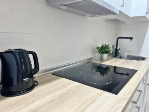 Cocina moderna en apartamento de Fuengirola con vitrocerámica de inducción, hervidor negro, fregadero y maceta sobre encimera de madera
