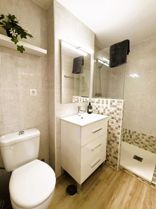 Baño moderno en apartamento de Fuengirola con tocador blanco, espejo grande, ducha a ras de suelo y paredes de azulejos beige
