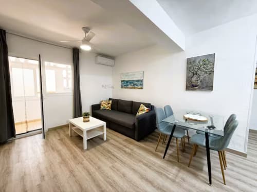 Moderno salón de apartamento en Fuengirola con sofá negro, mesa de comedor y acceso a balcón