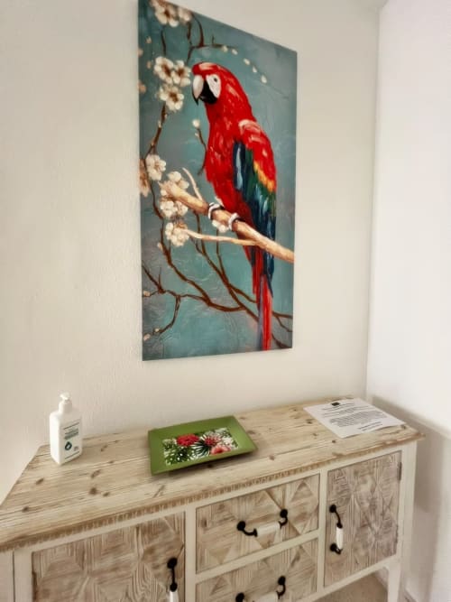 Interior luminoso de apartamento en Fuengirola con cómoda de madera, obra de arte con guacamayo rojo en pared turquesa y comodidades del hogar