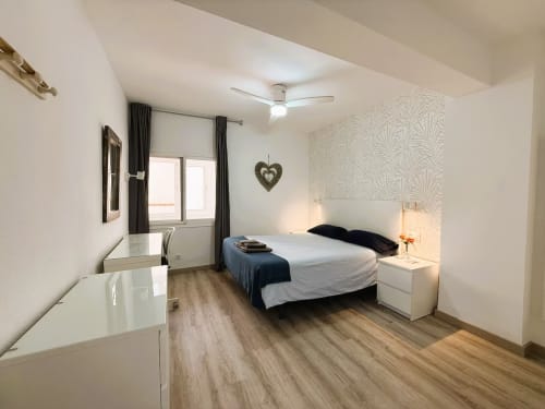 Moderno dormitorio en apartamento de Fuengirola con cama de matrimonio, escritorio, papel tapiz con diseño en cabecero y suelo de madera