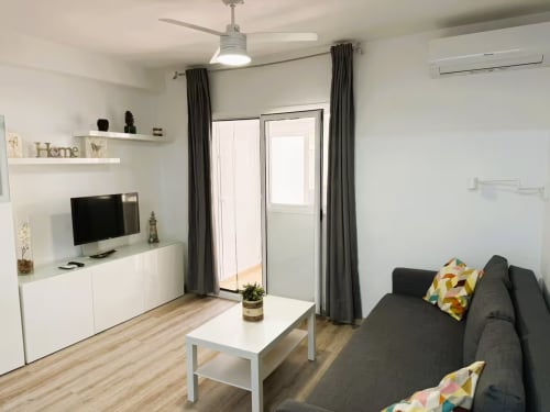 Salón moderno en apartamento de Fuengirola con sofá gris, televisor, mueble blanco y acceso a balcón
