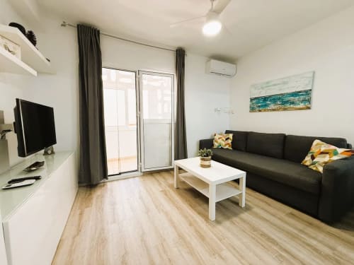 Moderno salón en apartamento de Fuengirola con sofá negro, televisor, mesita blanca y acceso a balcón
