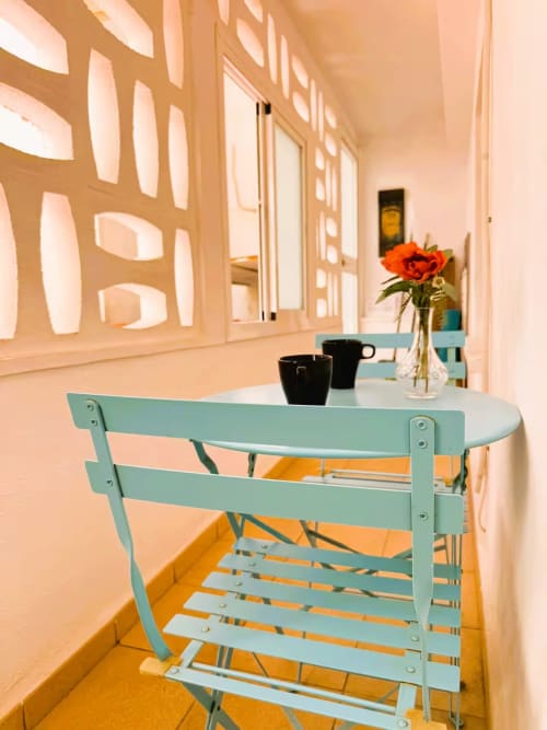 Balcón moderno en Fuengirola con silla turquesa, mesa de comedor, flor naranja en jarrón y decoración minimalista