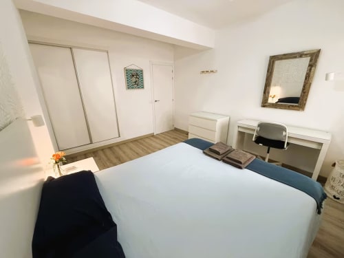 Luminoso dormitorio moderno en apartamento de Fuengirola con cama doble, muebles blancos, armario espejado y suelo de madera