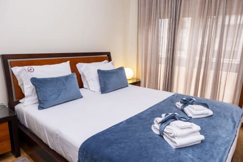 Quarto espaçoso do RH Charming Apartments em Barcelos com almofadas azuis, lençol branco e toalhas dobradas na cama