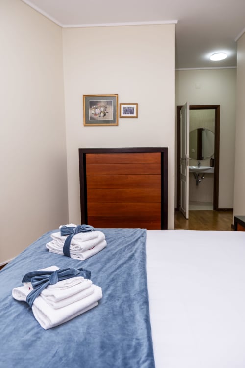 Bright bedroom at RH Charming Apartments in Barcelos with blue bed, folded towels, wooden headboard, and ensuite bathroom