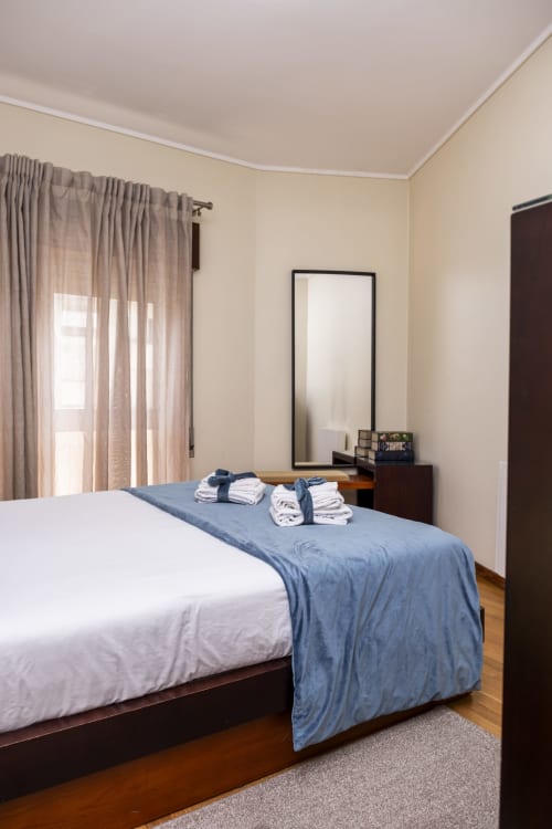Spacious bedroom at RH Charming Apartments in Barcelos with queen bed, blue runner, wooden nightstand, mirror, and beige