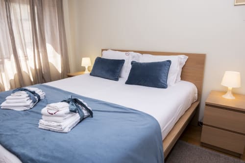 Bright bedroom at RH Charming Apartment in Barcelos with white bed, navy pillows, wooden frame, and bedside lamps