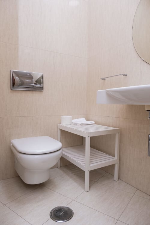 Modern bathroom at RH Charming Apartments, Barcelos featuring wall-mounted toilet, white shelving unit, and beige tile design