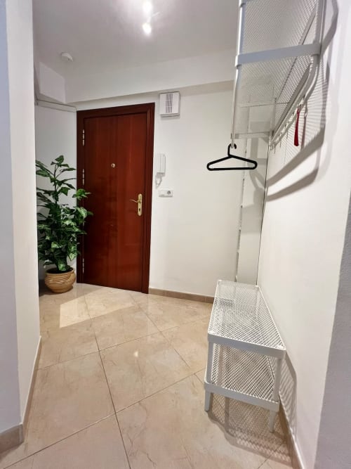 Recibidor moderno en Fuengirola con suelo de mármol, puerta de madera, paredes blancas y almacenamiento para ropa