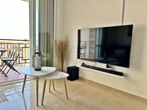Luminoso apartamento frente al mar en Fuengirola con televisor moderno, mesillas blancas y vistas a la terraza