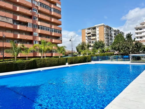 Piscina azul reluciente en complejo de apartamentos frente al mar en Fuengirola con edificios modernos y palmeras bajo cielo despejado