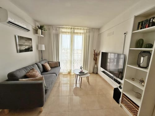 Sala de estar de apartamento moderno en playa de Fuengirola con sofá gris, TV, estanterías y vistas a la ciudad