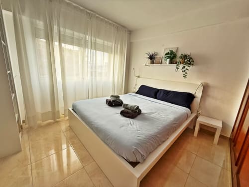 Luminoso dormitorio de apartamento de playa en Fuengirola con cama doble, cortinas traslúcidas, plantas en maceta y vistas a la ciudad